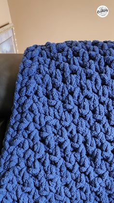 a blue crocheted blanket sitting on top of a black couch next to a brown chair