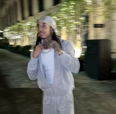 a woman in white is holding a cat and talking on her cell phone while walking down the street