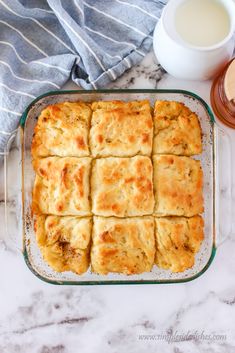 a casserole dish filled with biscuits next to a cup of milk and a napkin