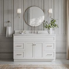 a white bathroom vanity with a round mirror above it and plants in vases on the counter