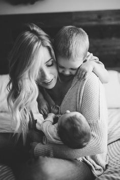 a woman holding a baby while sitting on top of a bed next to a man