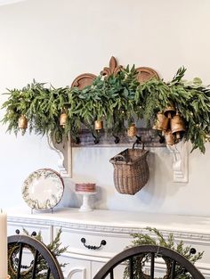 a christmas mantle with greenery, bells and plates hanging on the mantel above it