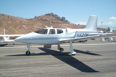 a small white plane sitting on top of an airport tarmac with mountains in the background