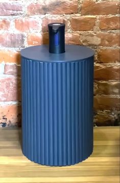 a blue trash can sitting on top of a wooden table next to a brick wall