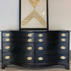 a large black dresser with gold handles and knobs on it next to a framed art piece