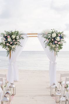 an outdoor ceremony set up on the beach with flowers and greenery in front of it