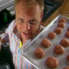 a man holding a tray full of doughnuts in front of him and looking at the camera