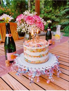 a birthday cake sitting on top of a wooden table next to two bottles of wine