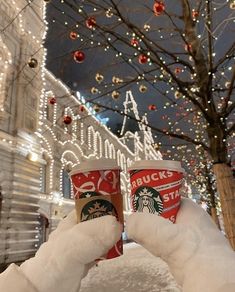 two cups of starbucks coffee are held up in front of a christmas - themed building