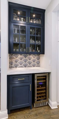 a wine cooler in the corner of a kitchen with dark blue cabinets and white counter tops