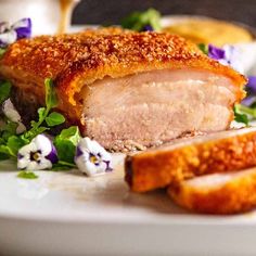 a white plate topped with meat covered in sauce and garnished with purple flowers