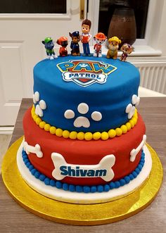 a three tiered birthday cake with toy figures on top and paw patrol logo on the side