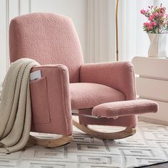 a pink rocking chair with a blanket on it and a flower pot in the background