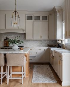 a kitchen with white cabinets and wooden floors is pictured in this image, there are two stools at the center of the island