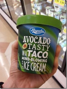 a hand holding an ice cream in front of a store display case filled with frozen yogurts