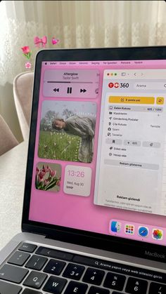 an open laptop computer sitting on top of a white table next to a pink flower