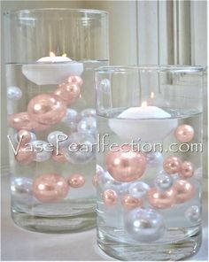 two glass vases with candles in them on a white tableclothed surface, one is filled with balls and the other has an ornament