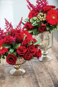 two vases filled with red flowers sitting on top of a wooden table next to each other