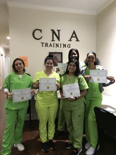 four women in green scrubs holding up their diplomas and posing for the camera