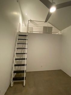 an empty room with a ladder leading up to the ceiling and a fan on the wall