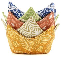 an assortment of colorful pillows stacked in a basket on top of each other with different patterns