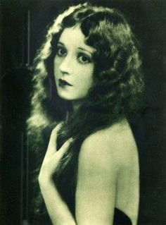 an old black and white photo of a woman with long curly hair wearing a dress