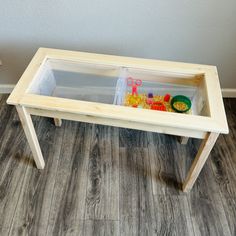 a child's wooden table with two trays on top and toys in the bottom