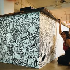 a woman sitting on the ground next to a large piece of art that is being painted