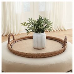 a plant in a white vase sitting on top of a round ottoman with rope handles