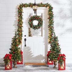 two christmas trees are decorated with red bows and lights in front of a white door