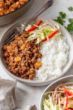 two bowls filled with rice, meat and veggies next to a bowl of coleslaw