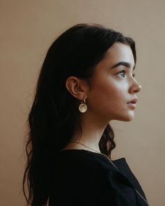 a woman with long black hair wearing gold earrings and a black top is looking off into the distance