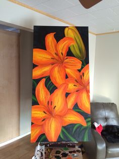 a painting of orange lilies on a canvas in front of a couch and chair