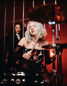 a woman with blonde hair sitting in front of a drum set and another person behind her