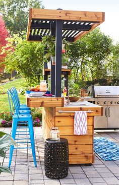 an outdoor kitchen with blue chairs and a grill in the back yard, surrounded by greenery