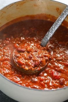 a ladle full of chili is being stirred by a wooden spoon in a pot