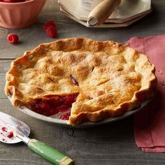 a pie sitting on top of a wooden table next to a bowl of raspberries