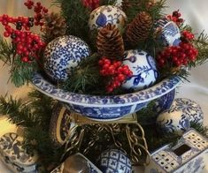 a blue and white christmas arrangement with pine cones, berries, bells and other ornaments