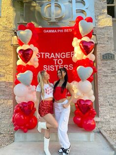 two young women standing in front of a large display of heart shaped balloons with the words strange to sisters on it