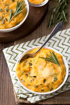 two bowls filled with mashed potatoes and garnished with rosemary, on top of a wooden table