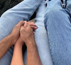 two people are holding hands while sitting on the ground with their feet crossed and one person is wearing blue jeans