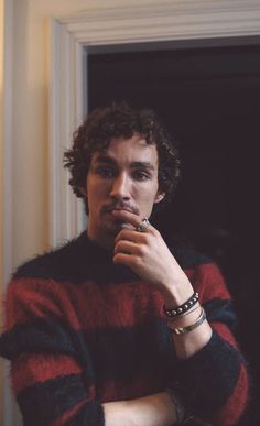 a young man with curly hair wearing a red and black striped sweater looking at the camera