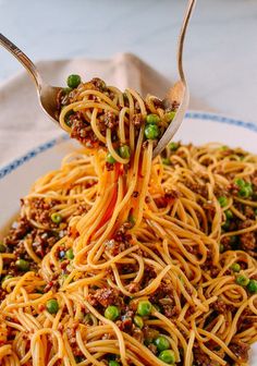 a fork is lifting up spaghetti from a white plate with peas and ground meat on it