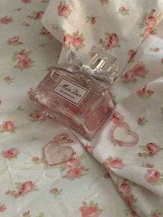 a pink perfume bottle sitting on top of a bed next to a white flowery blanket