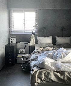 an unmade bed with white sheets and pillows in a bedroom next to a window