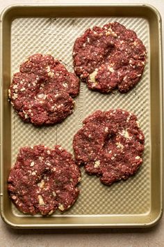 four hamburger patties sitting on top of a cookie sheet in a baking pan, ready to go into the oven