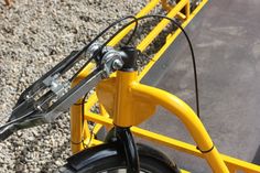 there is a yellow bike that is parked on the gravel and has two forks attached to it