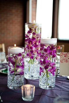 two vases filled with flowers on top of a purple table cloth next to candles