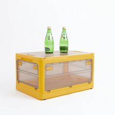 two green bottles are sitting on top of a yellow plastic case that is filled with ice