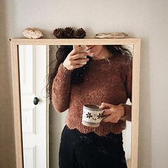 a woman taking a selfie in front of a mirror holding a coffee cup and looking at her reflection